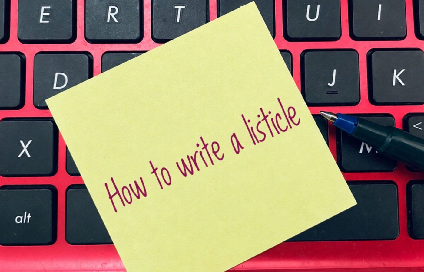 Sticky note reading "How to write a listicle" on a keyboard with a pen