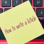Sticky note reading "How to write a listicle" on a keyboard with a pen