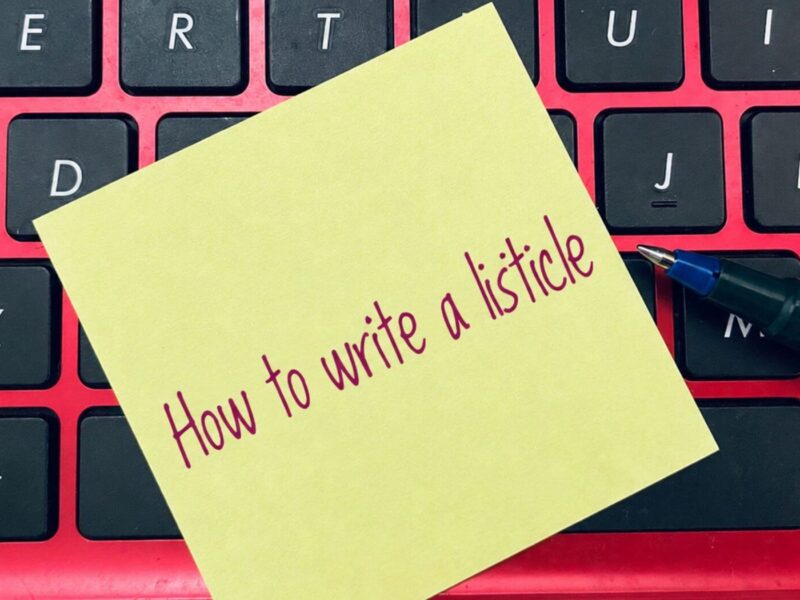 Sticky note reading "How to write a listicle" on a keyboard with a pen